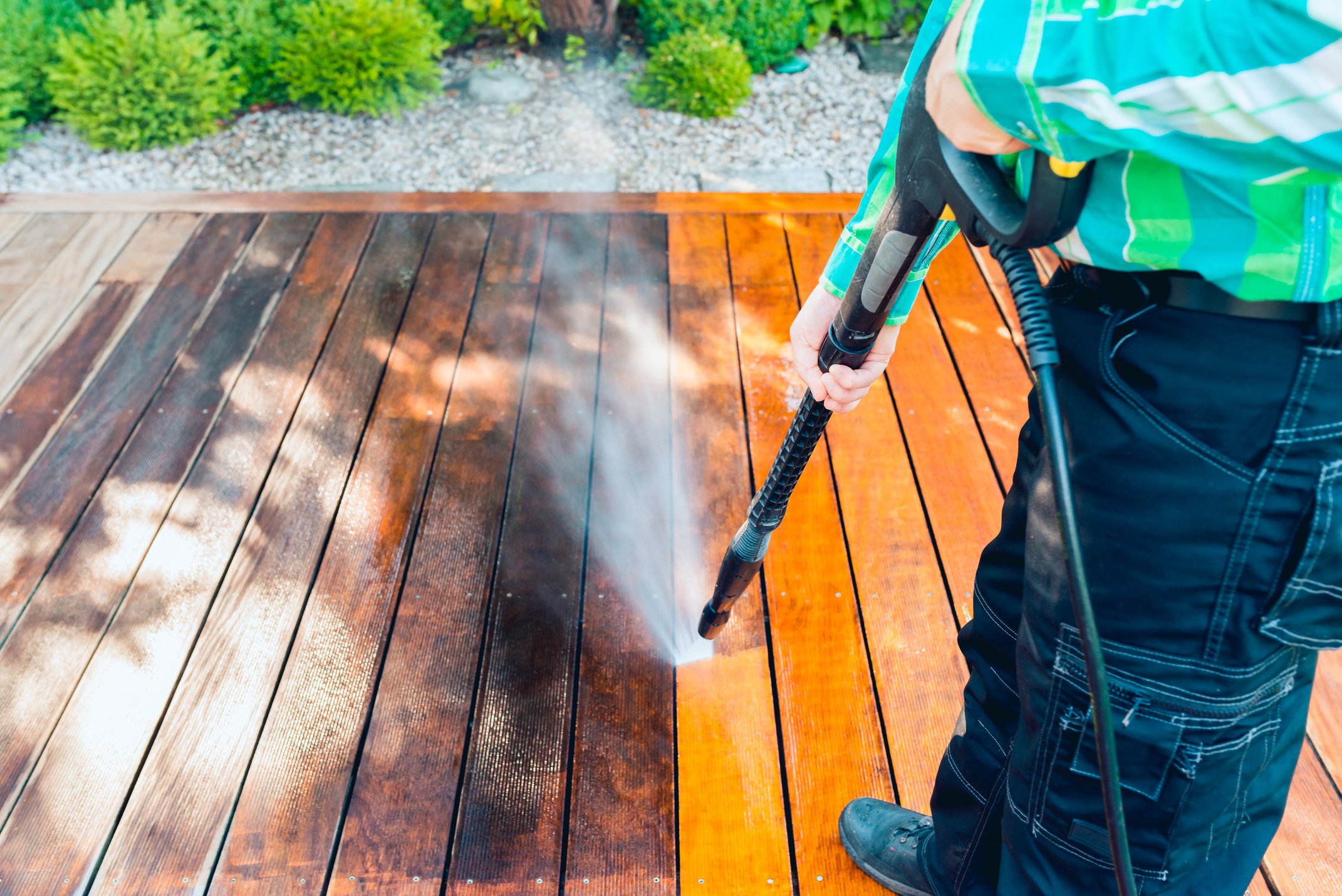 power washing - man cleaning terrace with a power washer - high water pressure cleaner on wooden terrace surface